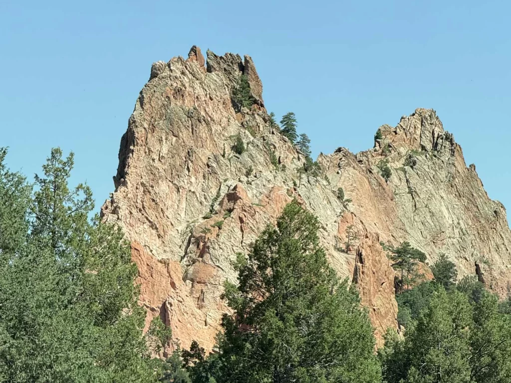 Jagged red sandstone rock formation in the Rocky Mountains with pine trees at its base.